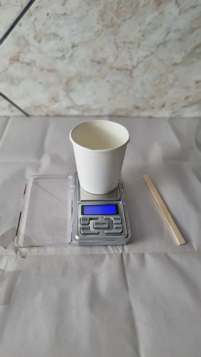 Balança digital com copo de papel, palito e base sobre a bancada