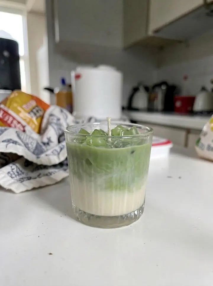 Vela artesanal verde em um copo canelado sobre uma mesa de cozinha